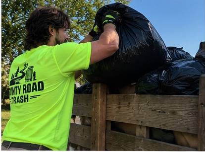 Loading a bag of trash into the County Road Trash trailer